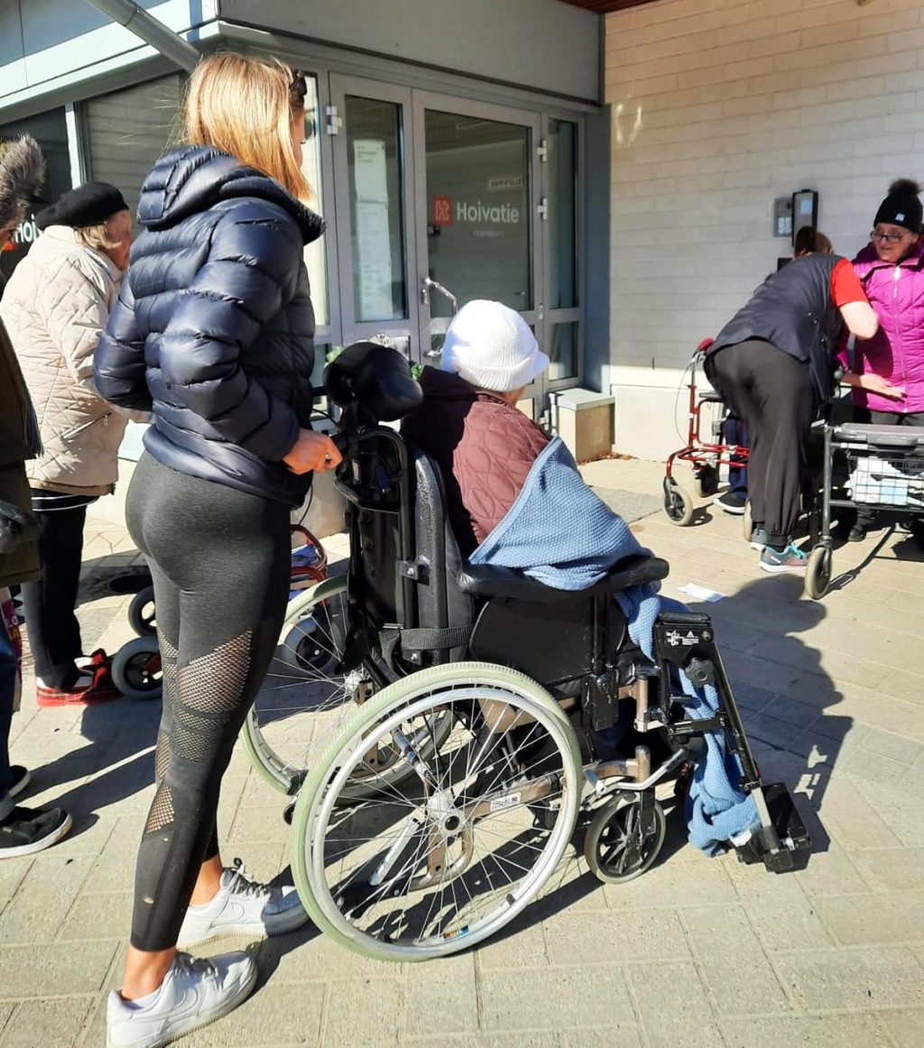 Nuori nainen työntää pyörätuolissa olevaa iäkästä naista.