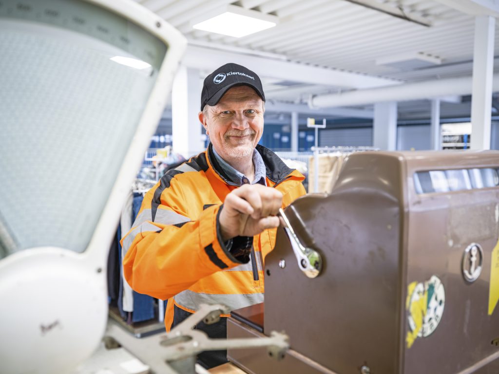 Mies oranssissa haalarissa kassakoneen ääressä.