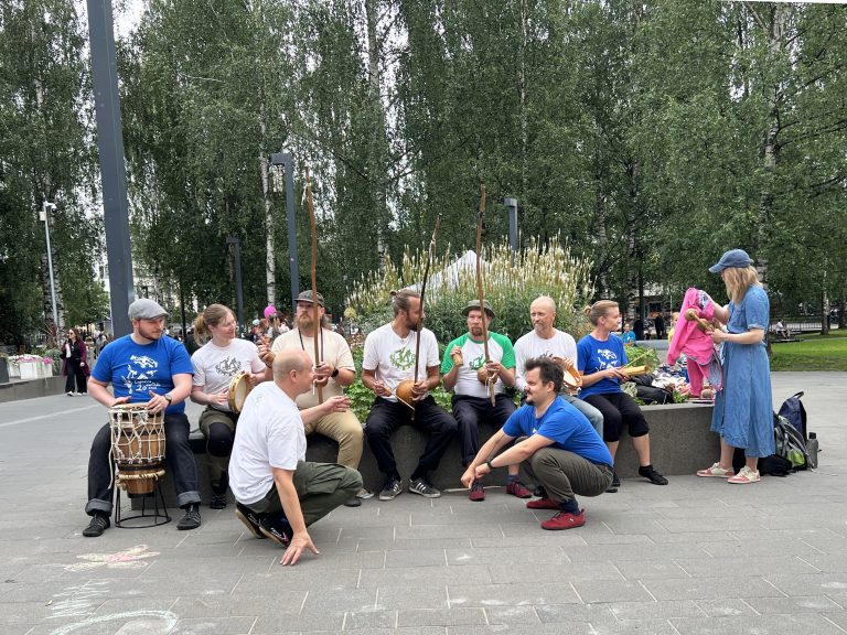 Kaksi copoeiran harrastajaa, taustalla penkillä muusikoita soittimien kanssa.