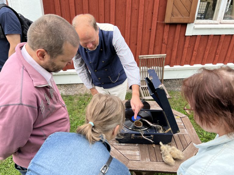 Mies esittelee vanhan levysoittimen toimintaa pienelle ryhmälle.