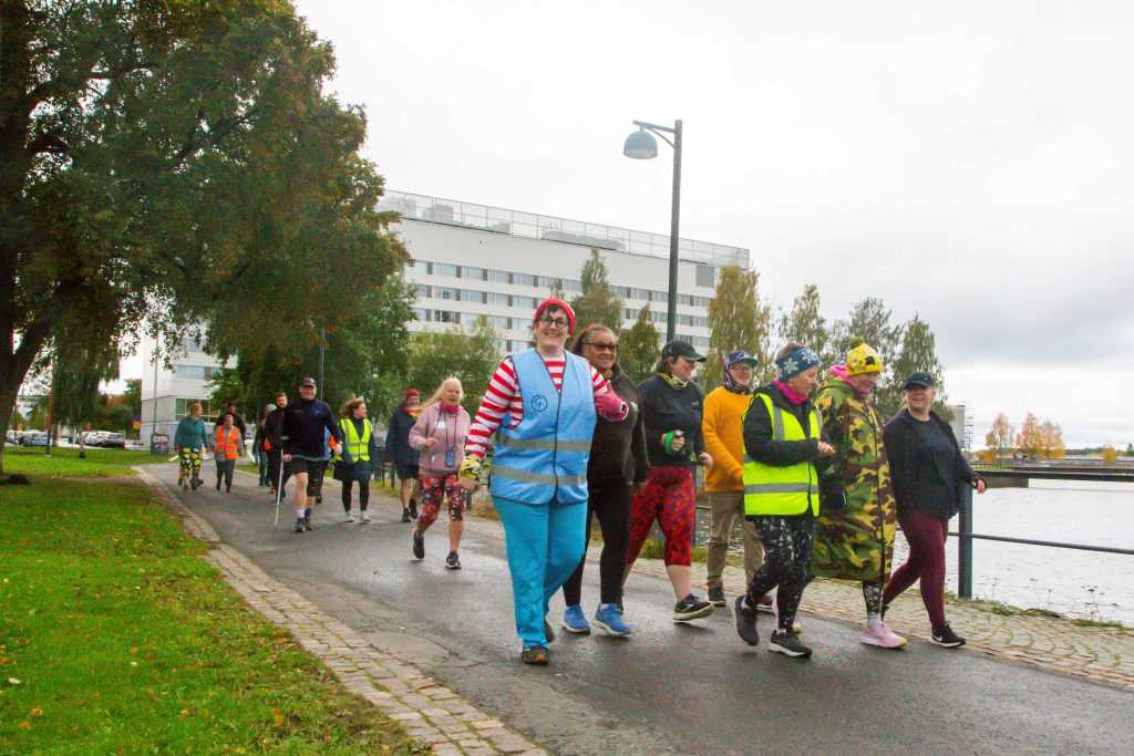 Värikkäästi pukeutuneita kävelijöitä rantatiellä.