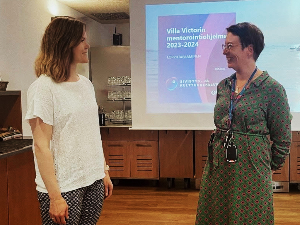 Two women smiling and talking in a classroom.