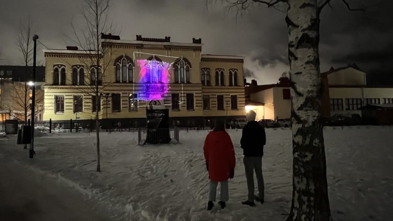 Mies ja nainen katselevat koulun seinään heijastettua valotaidetta.