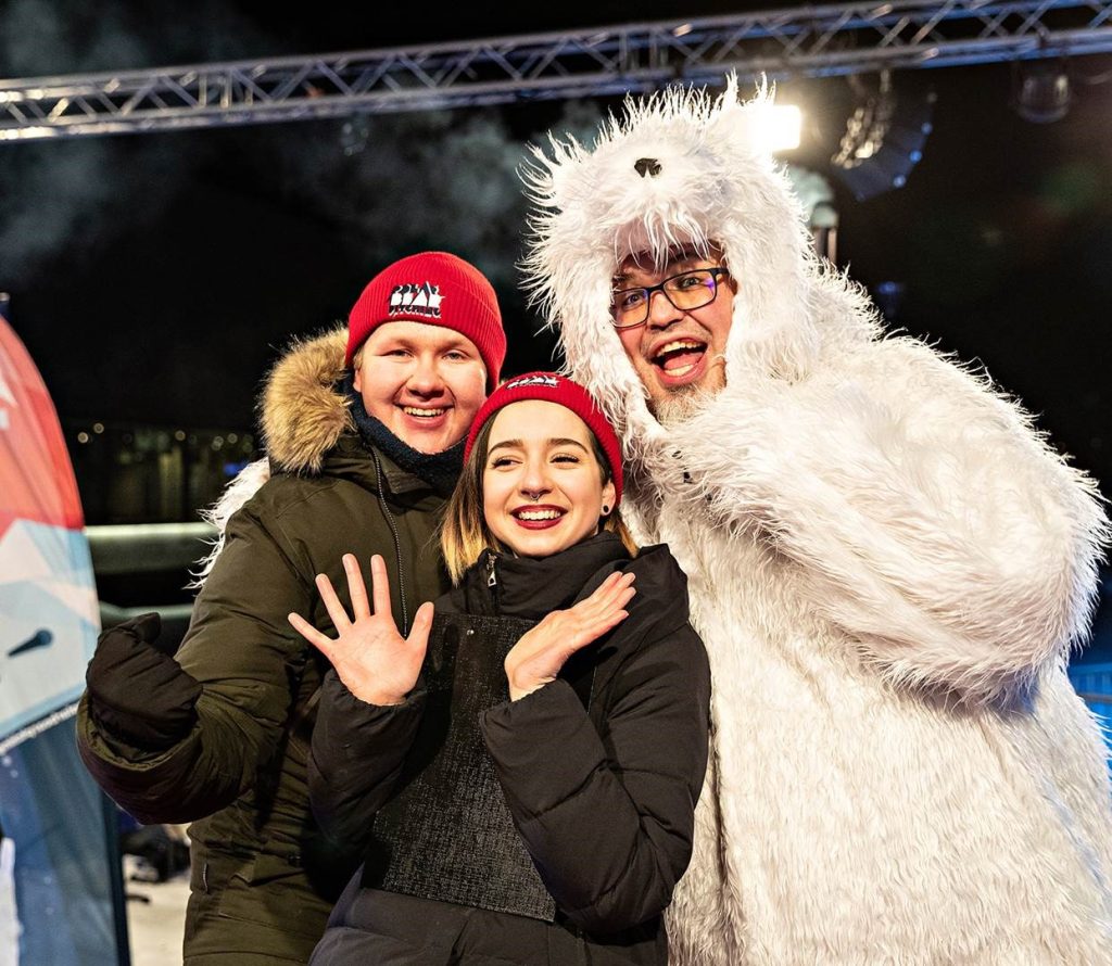 Nainen ja kaksi miestä poseeraavat iloisesti, toinen miehistä jääkarhupuvussa.